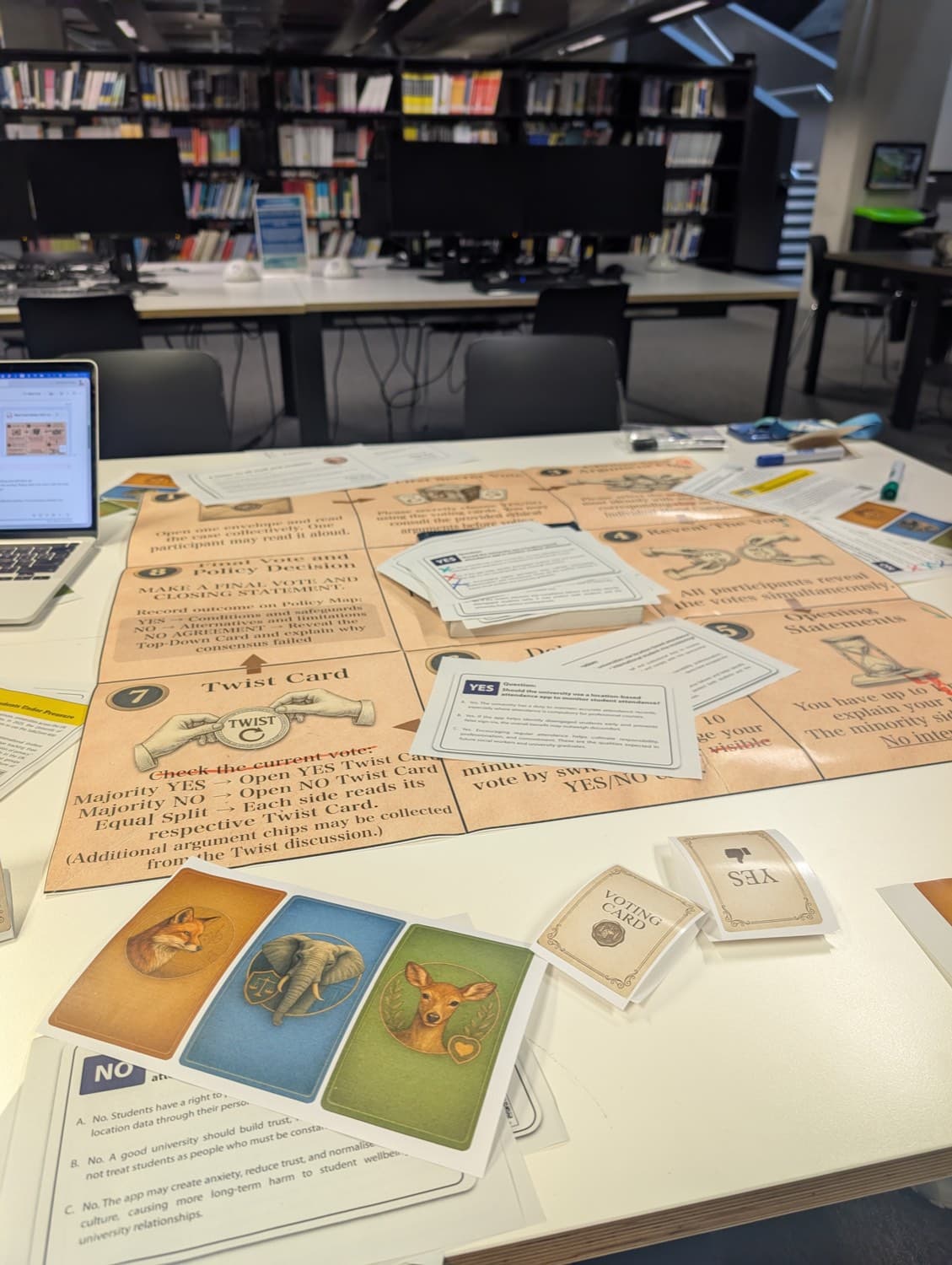 The ethixCube board on a library table, twist and voting cards laid across it, the three animal reasoning cards in the foreground
